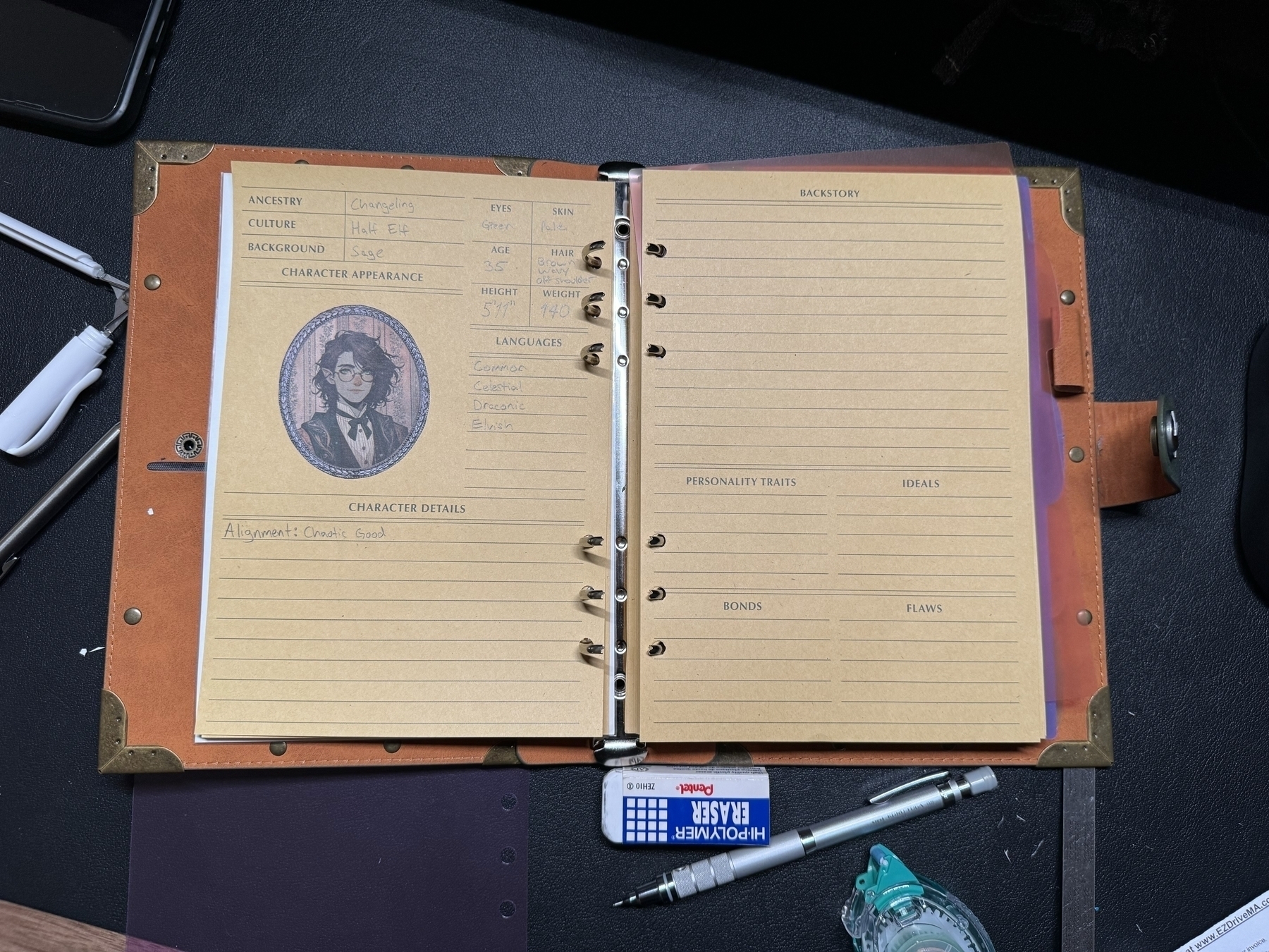 An image of an open binder with a role-playing game character sheet. On the left, there's an image of a nonbinary character with dark hair and glasses, surrounded by information like ancestry (Changeling, Half-Elf) and background (Sage). The character's alignment, "Chaotic Good," is noted below. The right page, meant for the character's backstory and traits, is blank. A pencil, a roll of double sided tape, and an eraser lie on the desk (which is a horrible mess just out of frame).