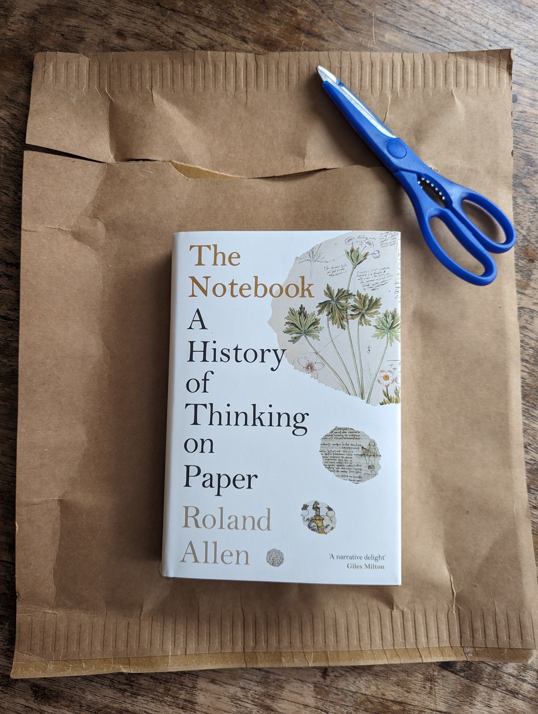 The cover of Roland Allen’s book, The Notebook. A History of Thinking on Paper. Beneath it lies the brown paper envelope it arrived in, and beside it sits the blue pair of scissors that opened the package.