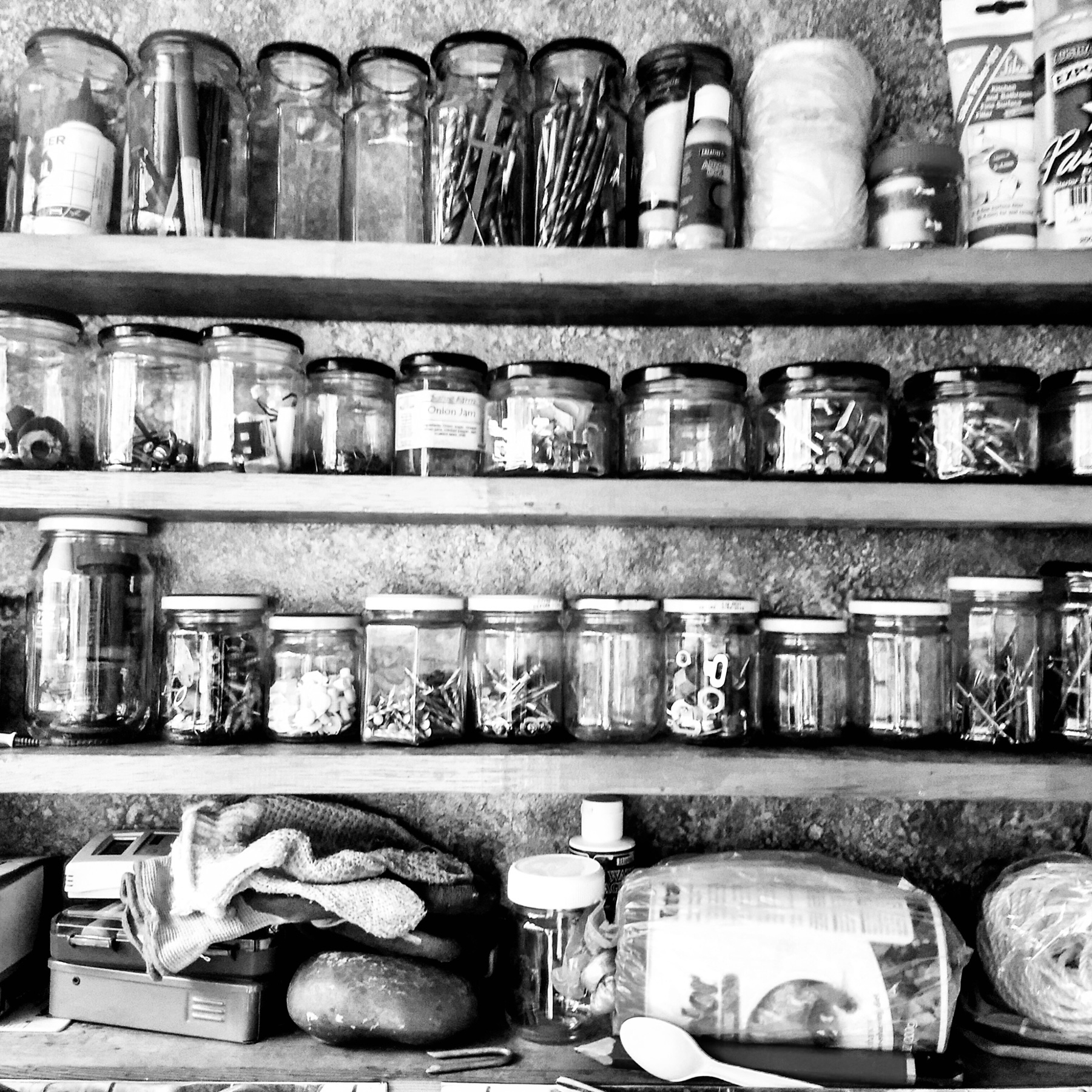 A black and white image of a set of shelves with jars of screws, nuts and bolts.