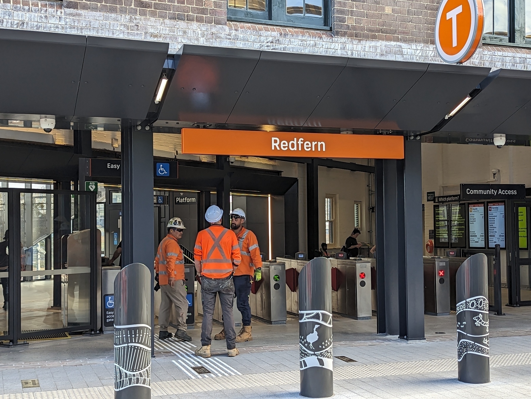 Three construction workers stand at the newly opened Southern entrance to Redfern Station in Sydney&10; Bollards in the foreground show Aboriginal art, recognising Redfern's strong Indigenous culture, politics and heritage.