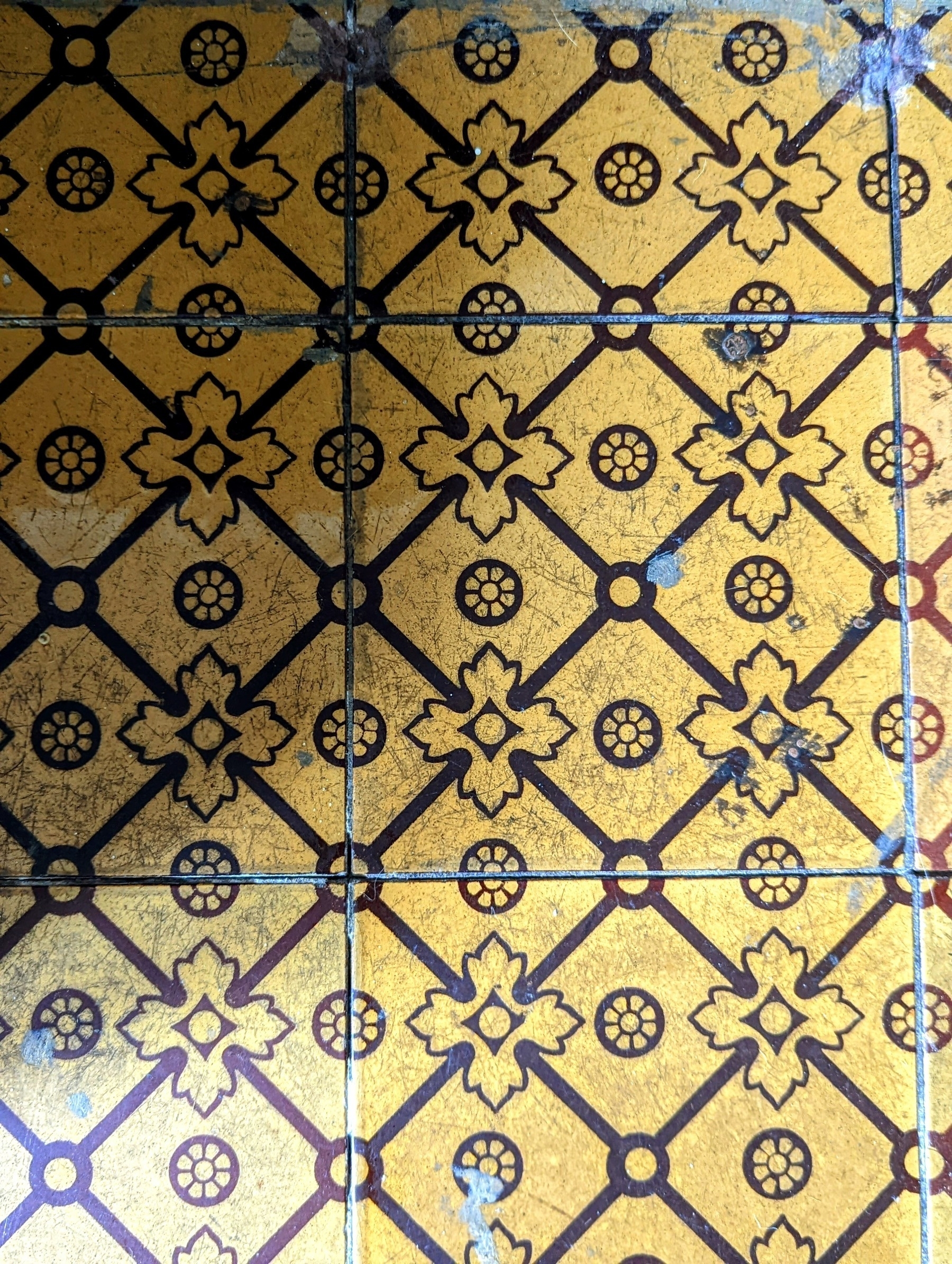 A close-up of antique mustard-coloured hearth tiles, with a diamond motif in brown. 