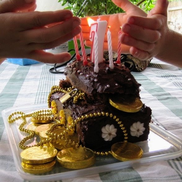 A chocolate birthday cake in the shape of a treasure chest, complete with gold coins and candles. 
