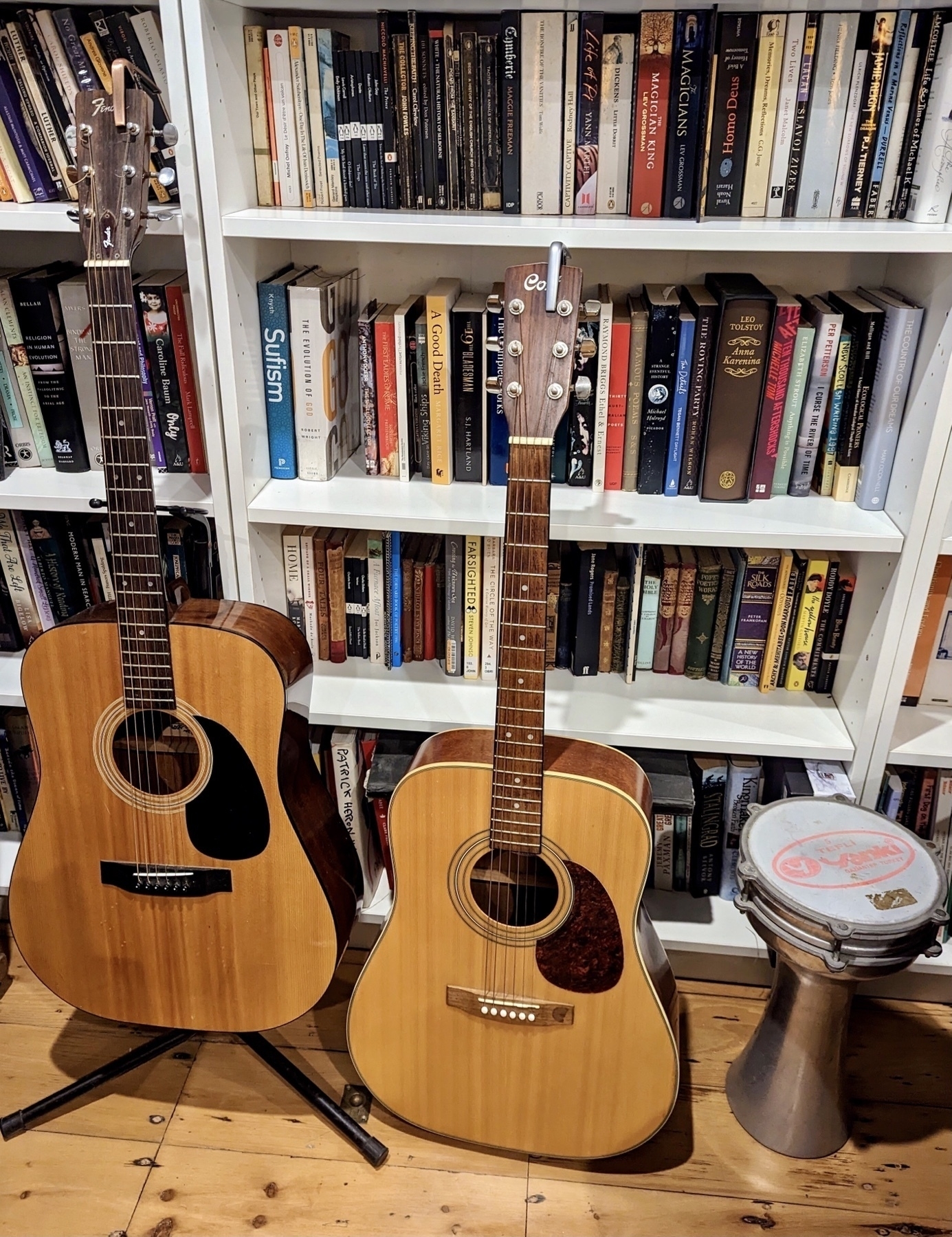 Two acoustic guitars and a Turkish drum in front of a bookcase.
