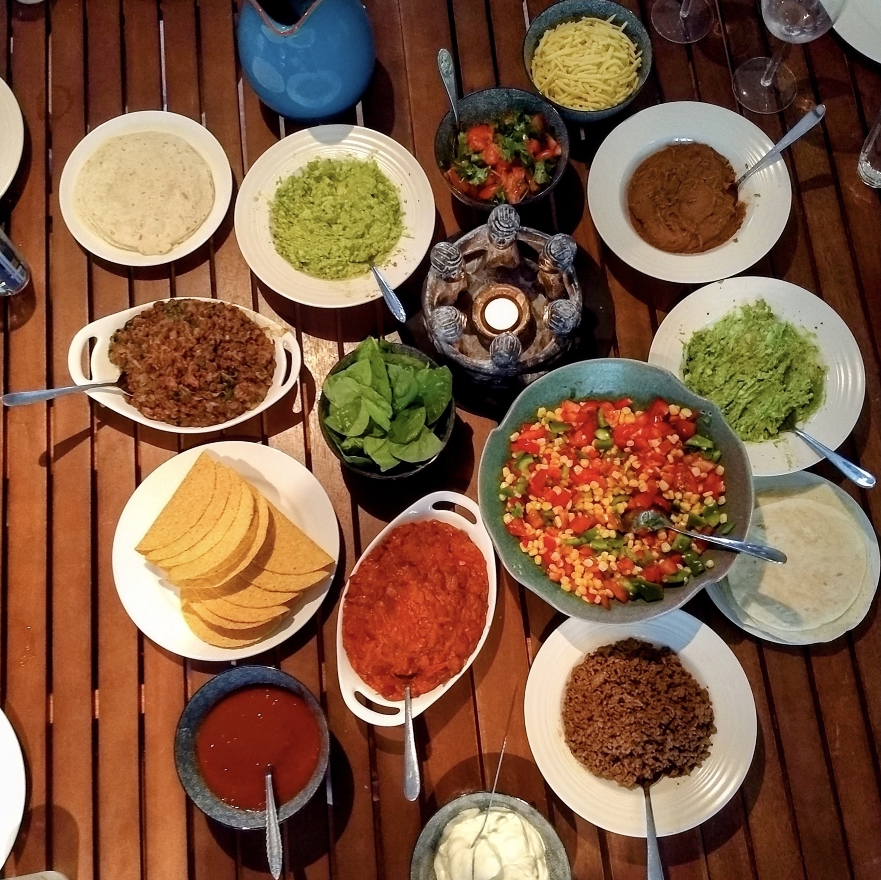 Viewed from above, a wooden table laid out with the many varied dishes of a Mexican-style meal