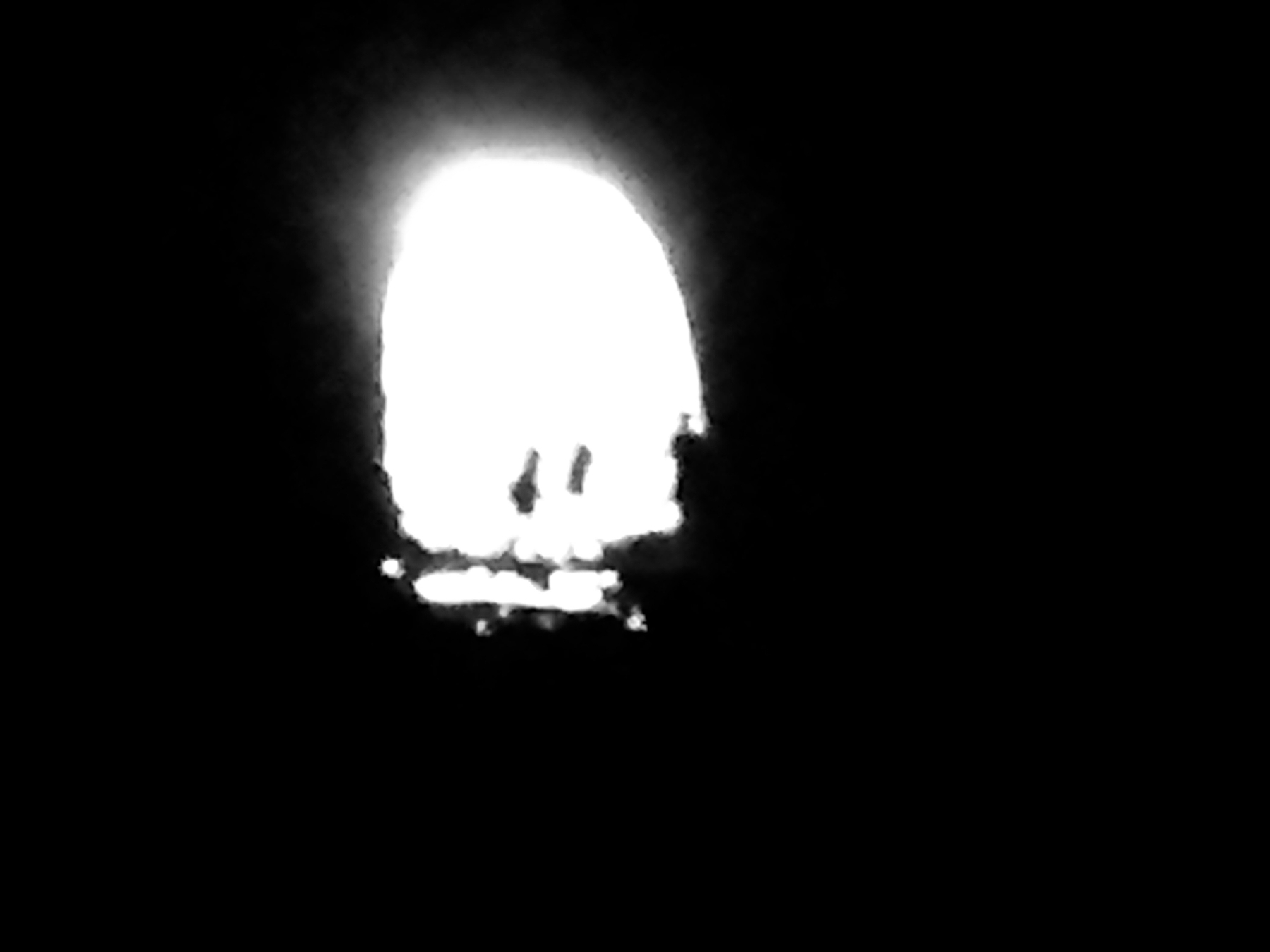 A low-resolution, high contrast photo of the light at the end of a disused rail tunnel. At the entrance, two or three figures are barely visible.