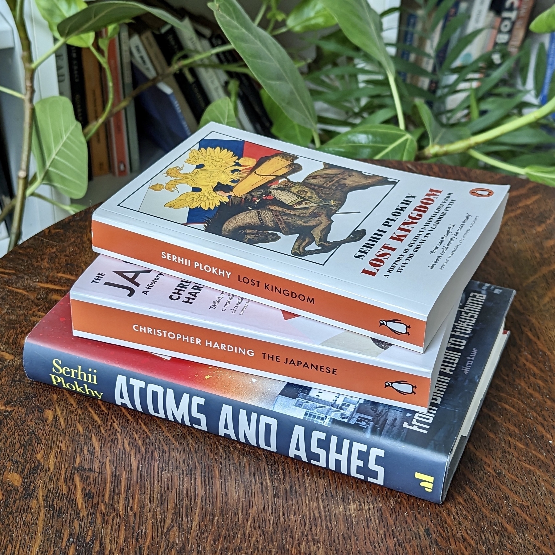 A small pile of three books on a wooden table.