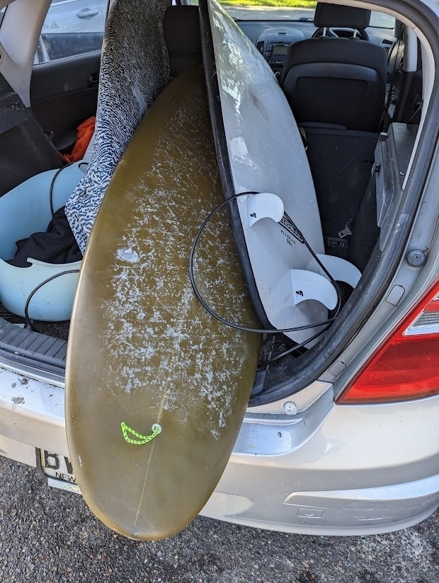 An open car trunk, barely containing three surfboards.