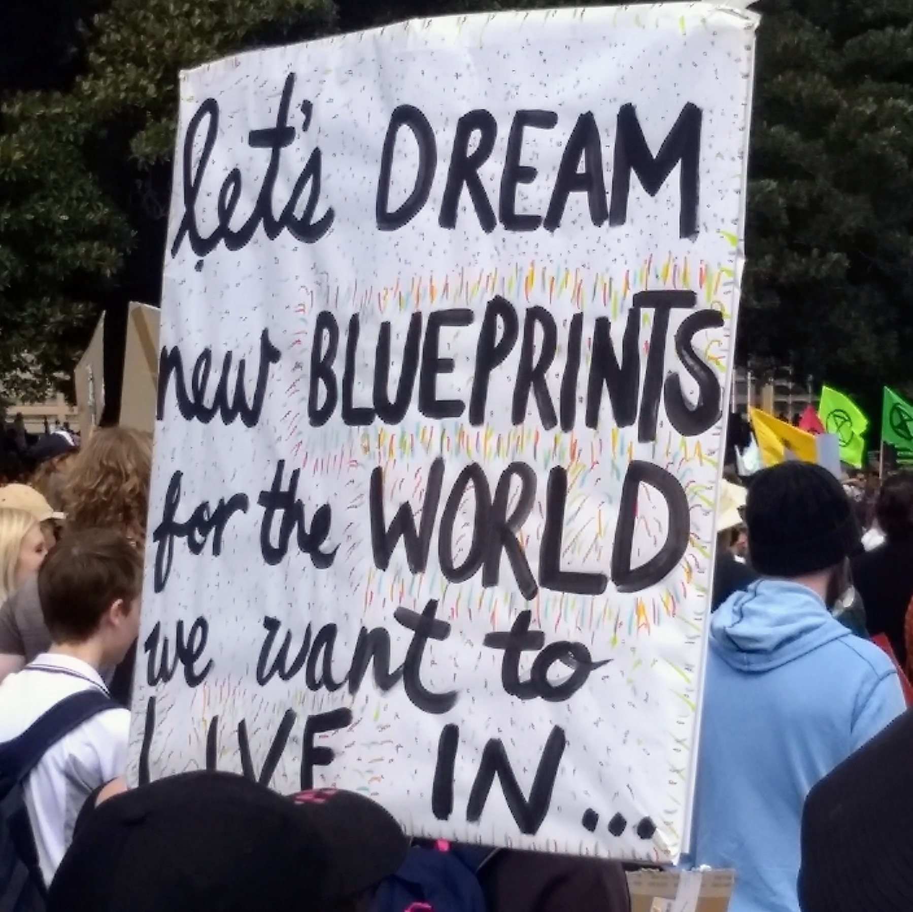 A demonstrator at a Sydney climate change protest holds up a hand-written sign that reads: Let's dream new blueprints for the world we want to live in.