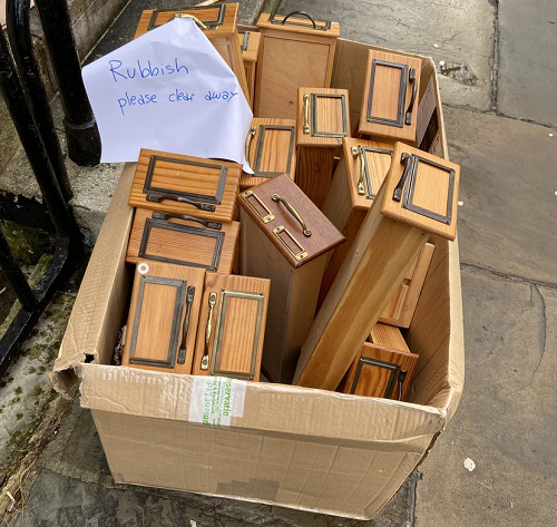 A cardboard box on the street, containing a set of card index drawers for disposal. An attached hand-written note says: Rubbish - please clear away.