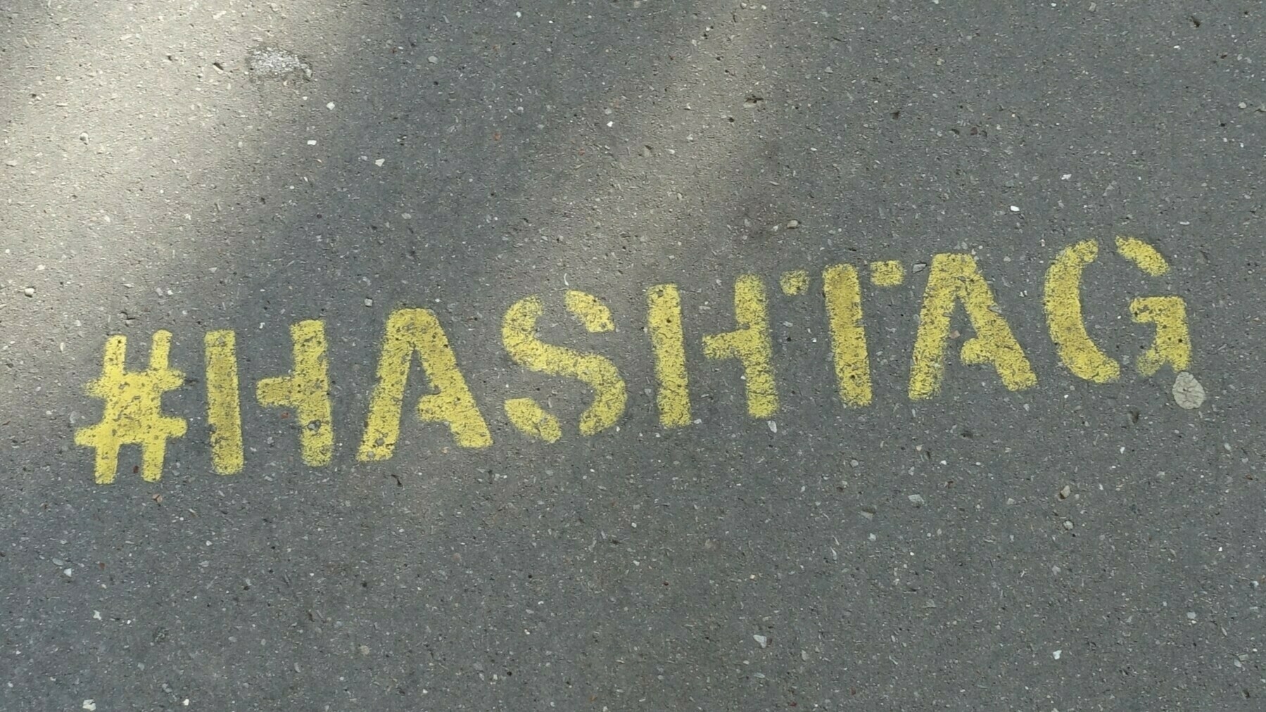 A yellow stencil on a road surface reads: #hashtag