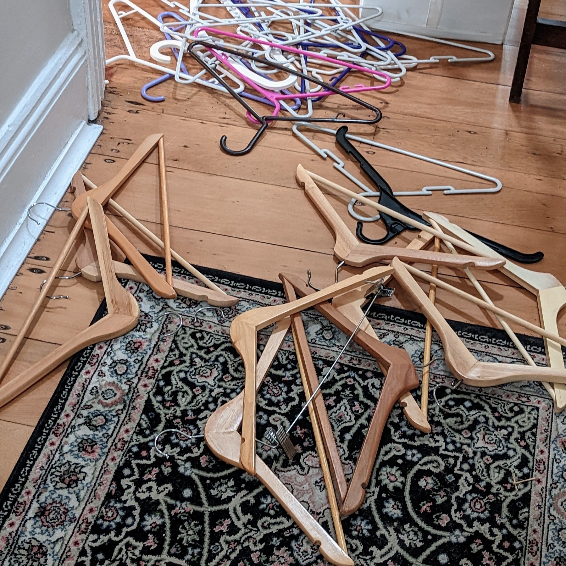 Coat-hangers are strewn about the wooden floor, with a rug in the foreground.
