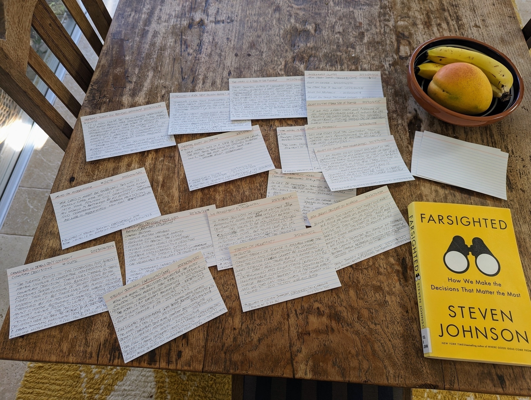 The book Farsighted by Steven Johnson sits on a wooden table top. Beside it lies spread out a group of index cards with hand-written notes.