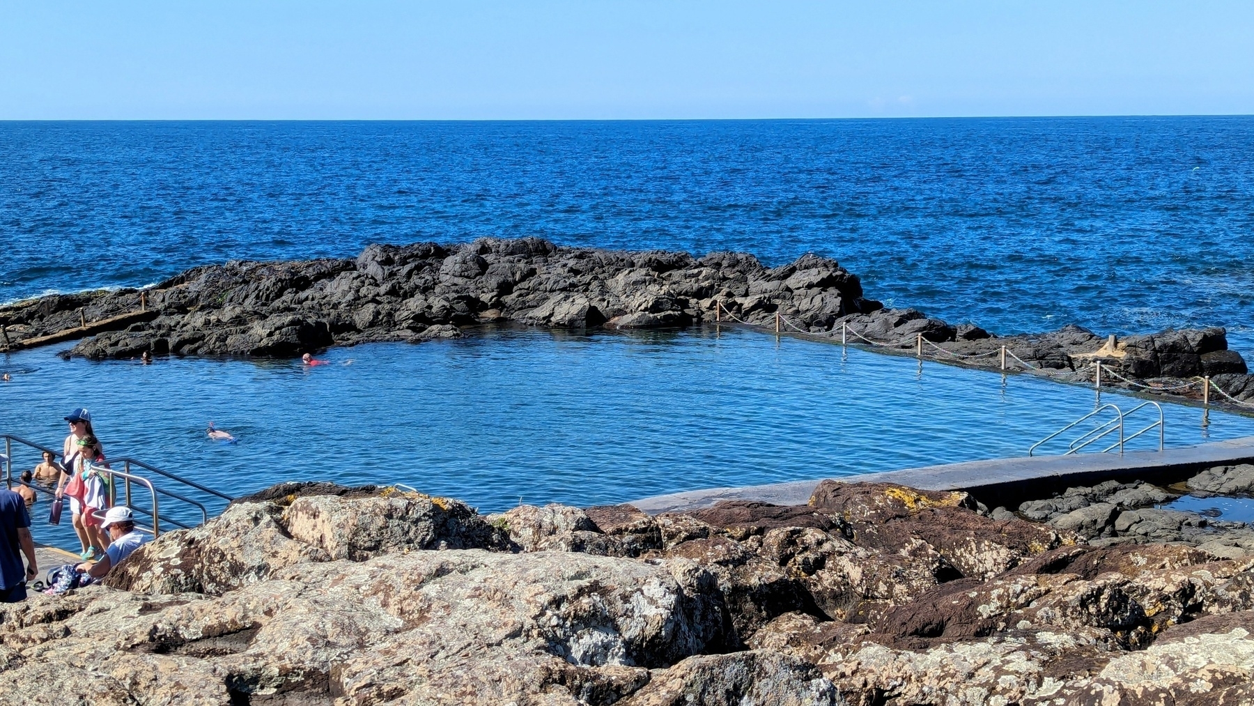A rock swimming  pool with the ocean in the background. The water looks very blue.
