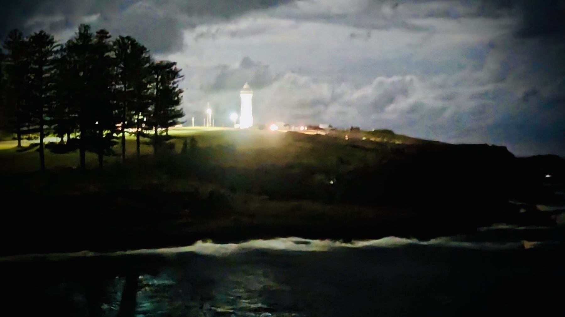 A lighthouse glowing brightly on a dark headland 