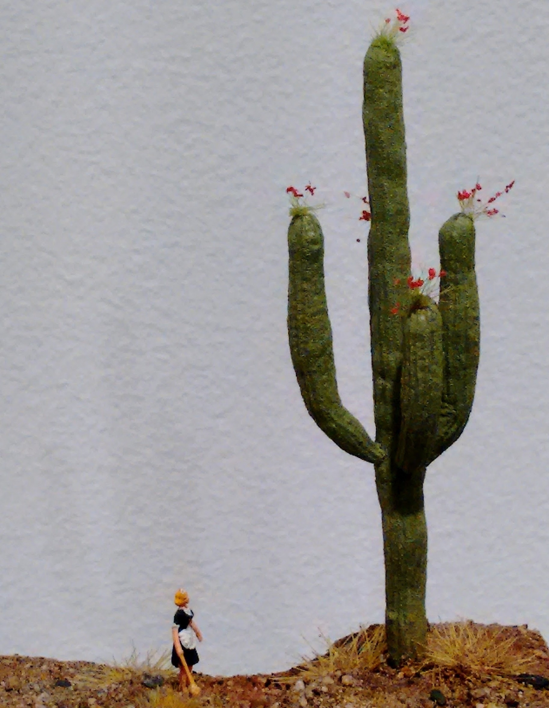 A model diorama of a woman looking at a large cactus. It’s an artwork by Karl De Waal.
