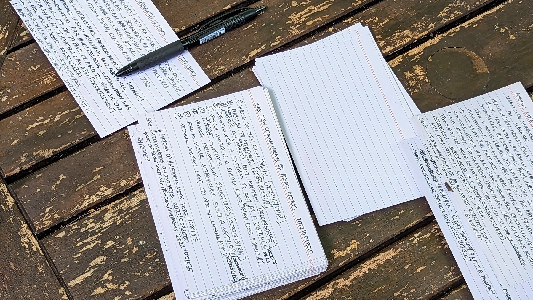 Handwritten note cards spread on a wooden table. There's a black pen beside them.