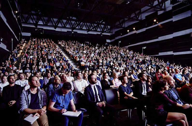 An audience of 1,000 is seated in an auditorium, attentively facing a stage or speaker.