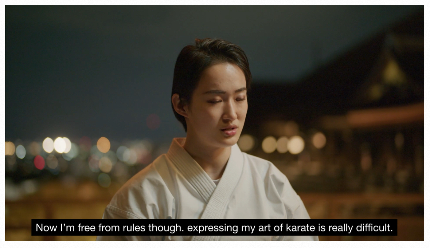 The karate champion Kiyou Shimizu is speaking about her experience with karate, with the Kyoto cityscape blurred in the background.