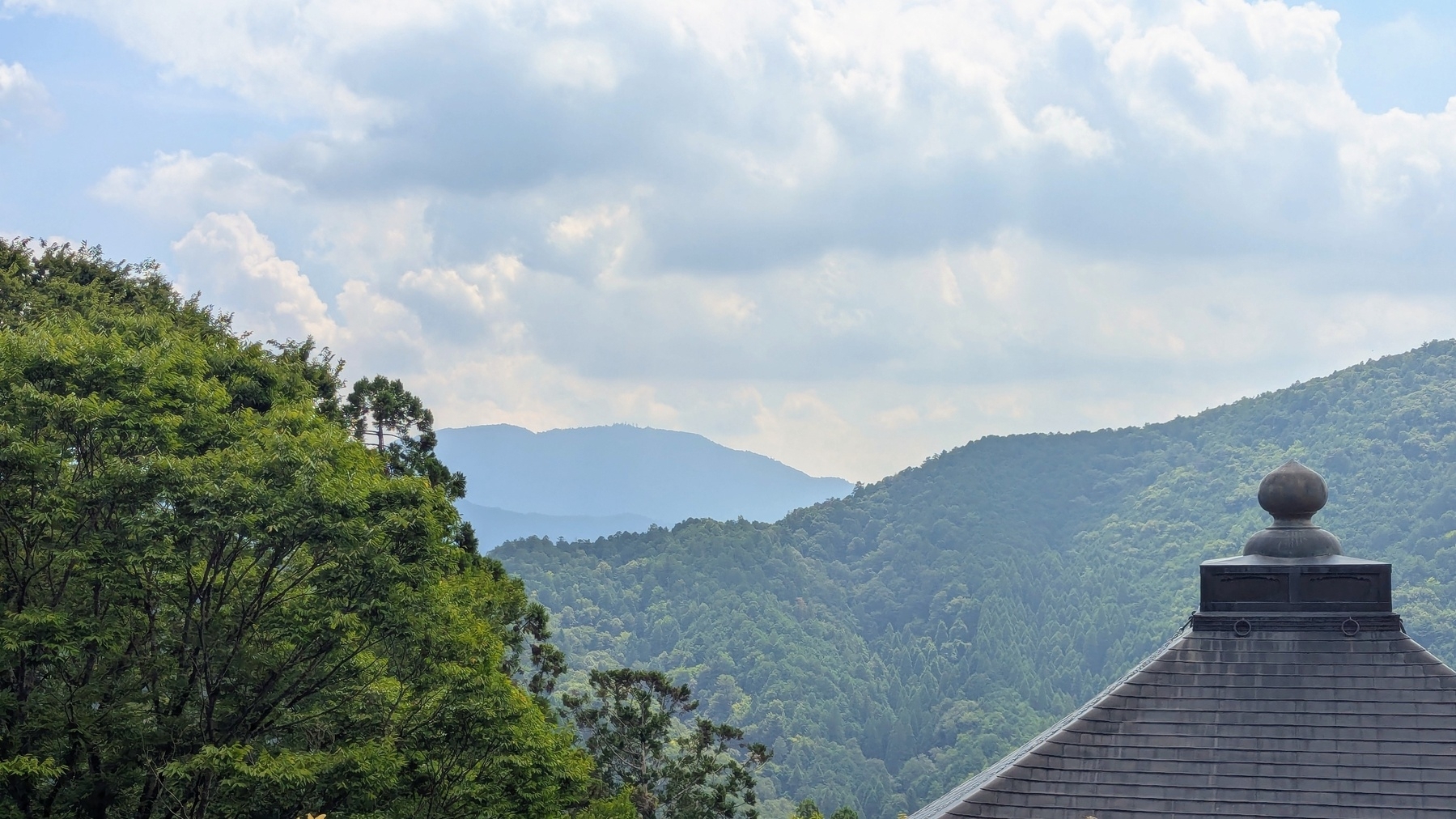 A lush, mountainous landscape with cloudy skies and a temple roof in the foreground.