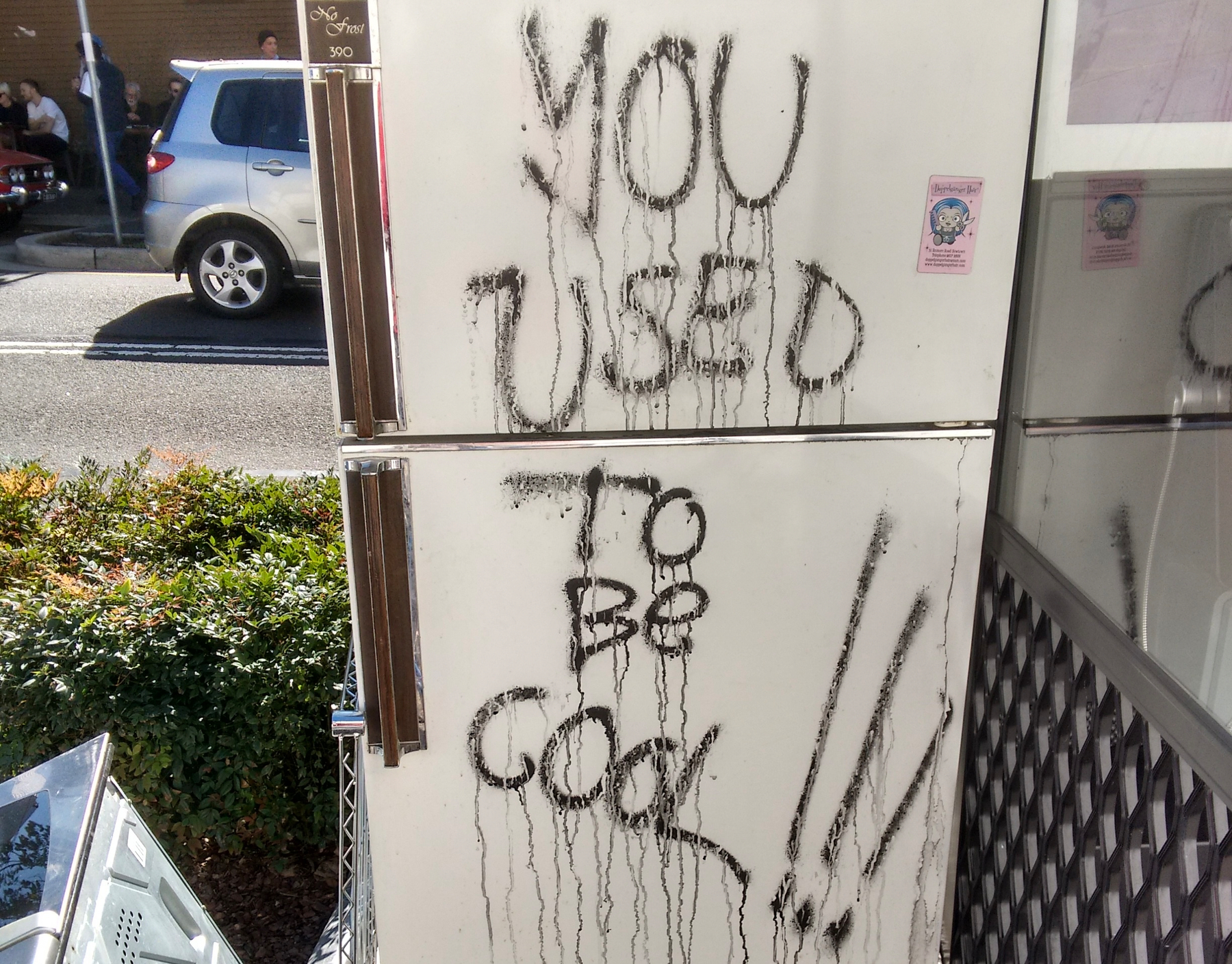 A white fridge on the street has graffiti that reads YOU USED TO BE COOL!!! written in black paint.