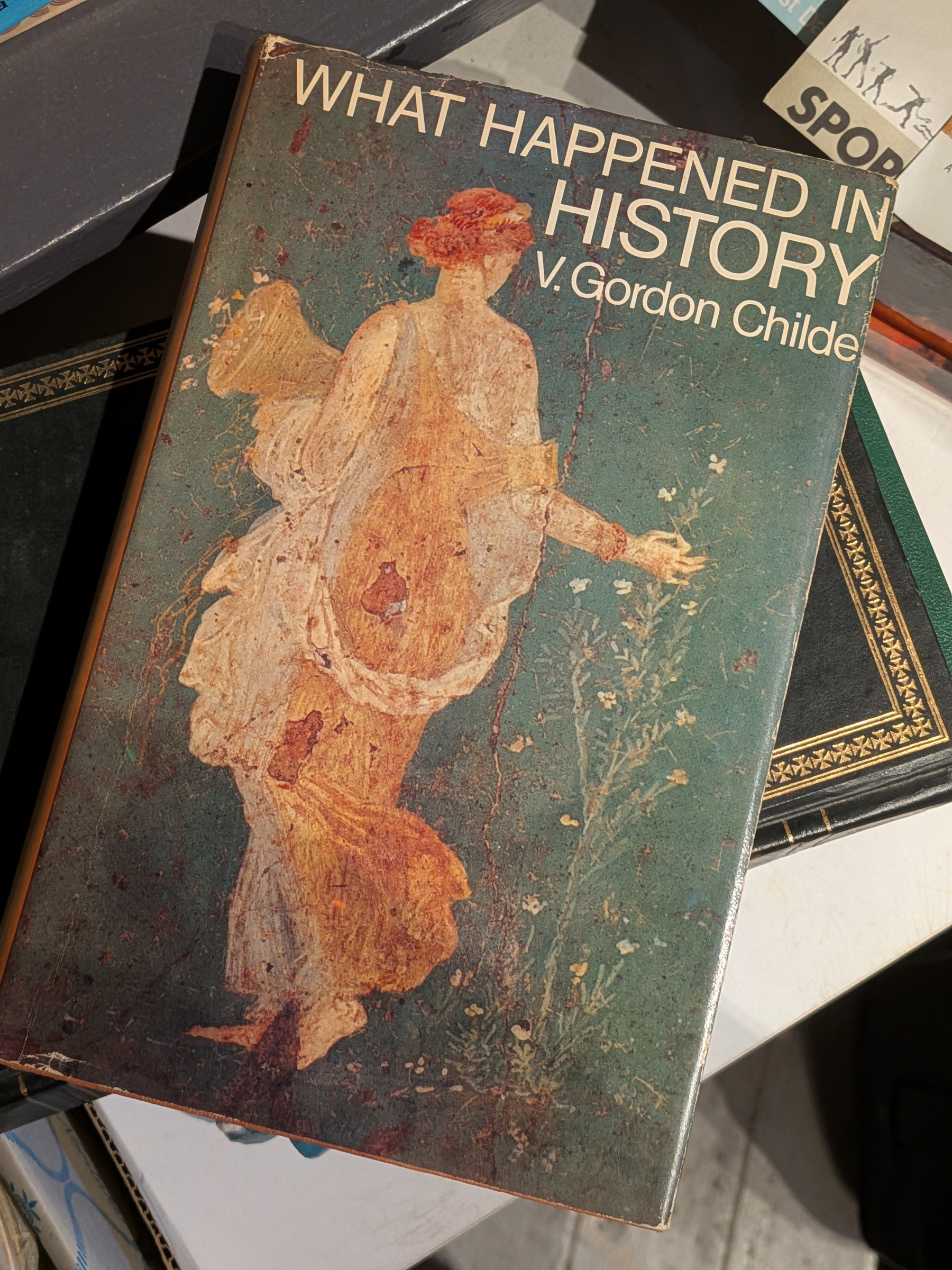 A worn book titled What Happened in History by V. Gordon Childe features an classical-style illustration of a woman on its cover.