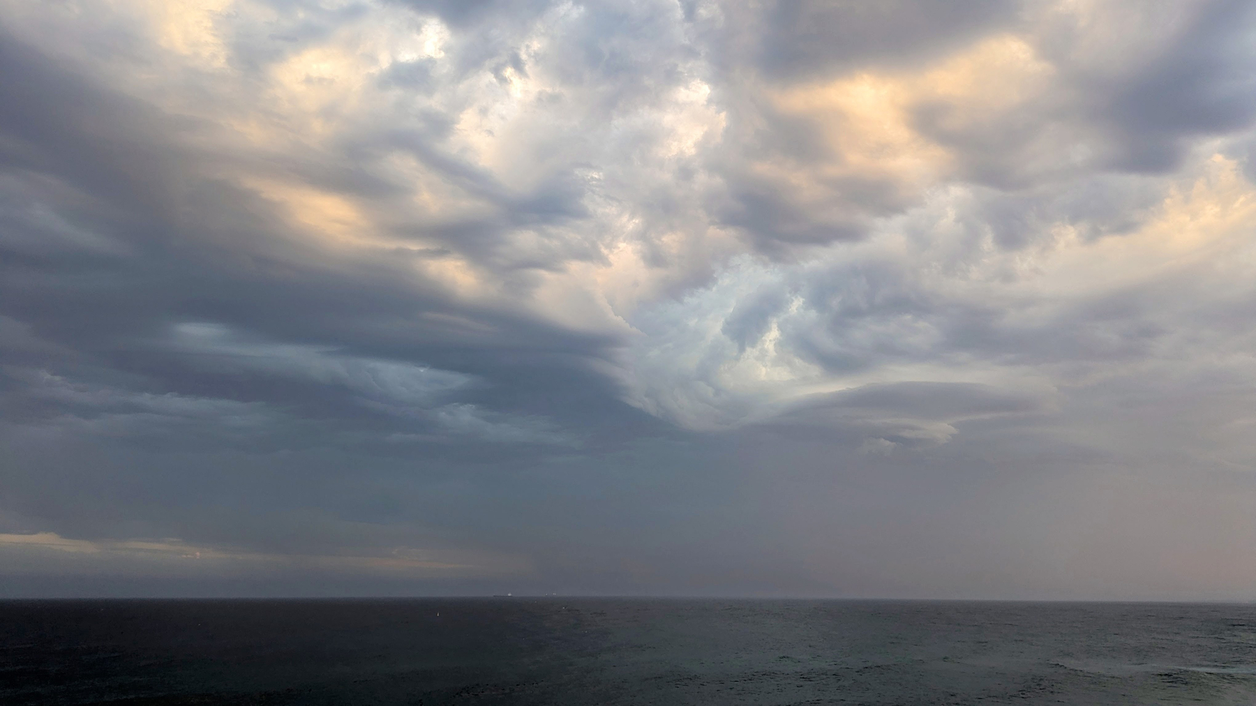 A vast, cloudy sky looms over a calm ocean, creating a serene and moody atmosphere.