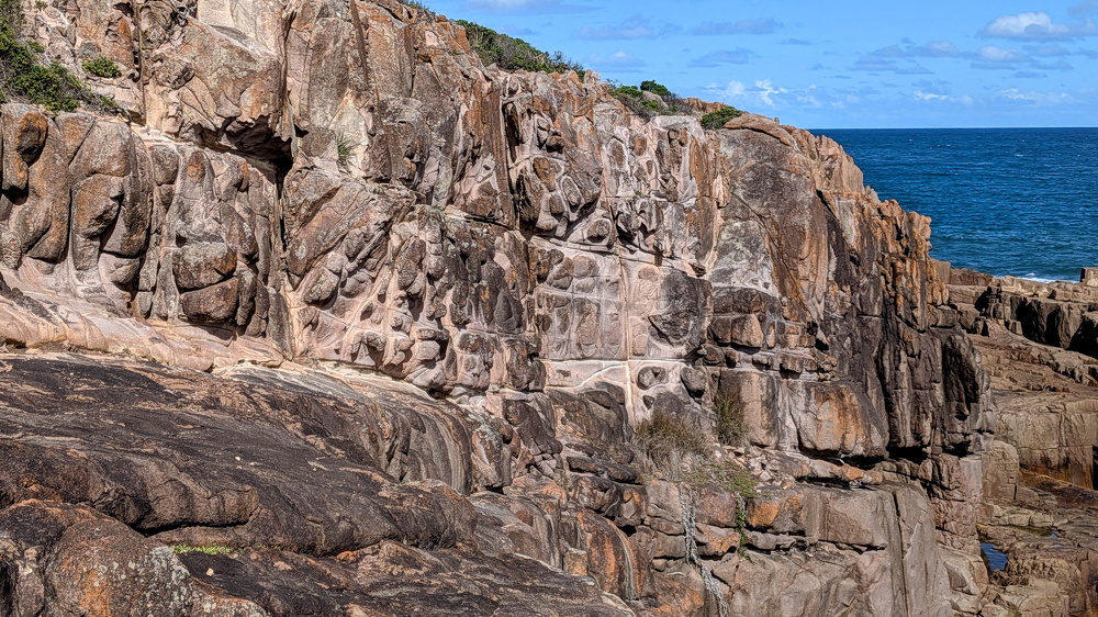 A rocky cliffside overlooks the blue ocean under a partly cloudy sky.
