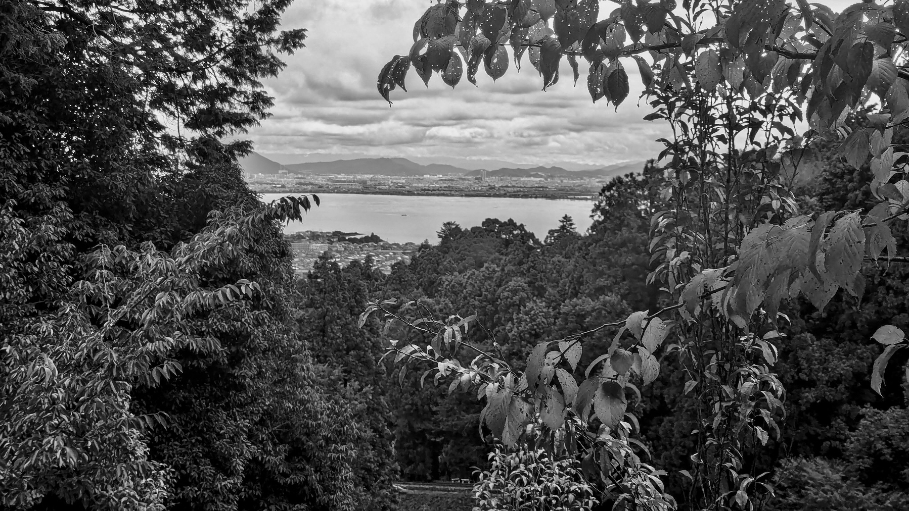 A scenic view over Lake Biwa near Kyoto showcases lush foliage framing a distant body of water and mountains in the background.