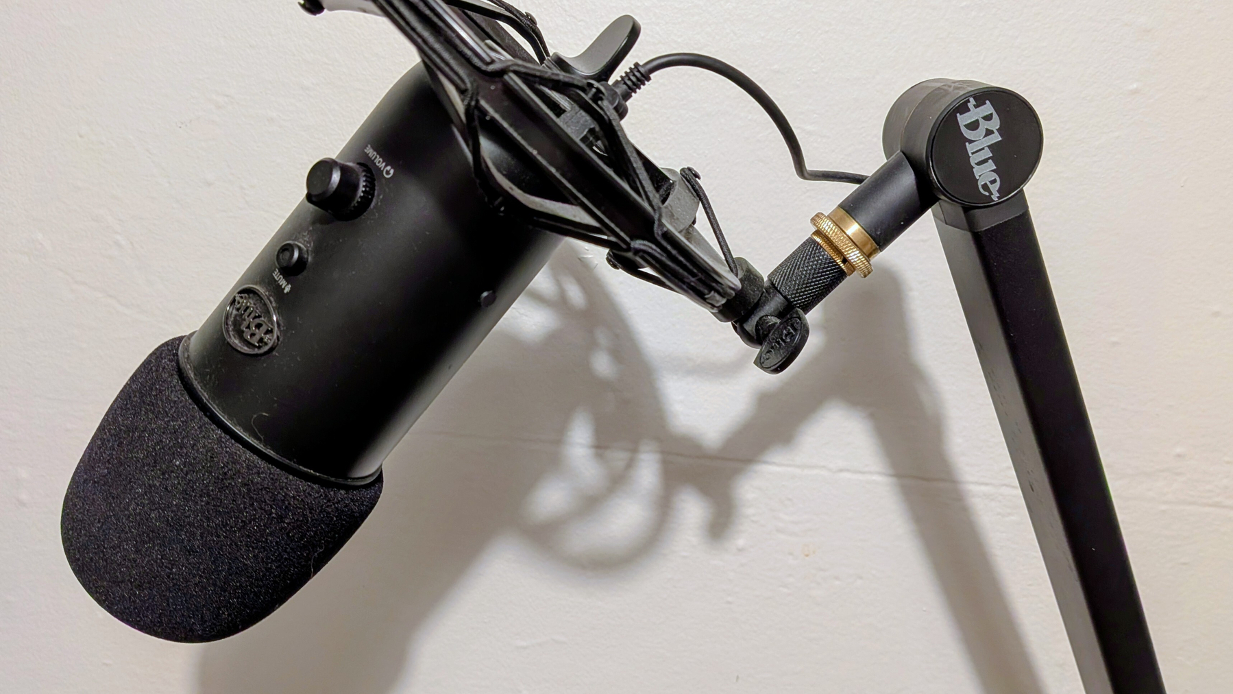 A microphone is mounted on a black adjustable arm against a white wall.