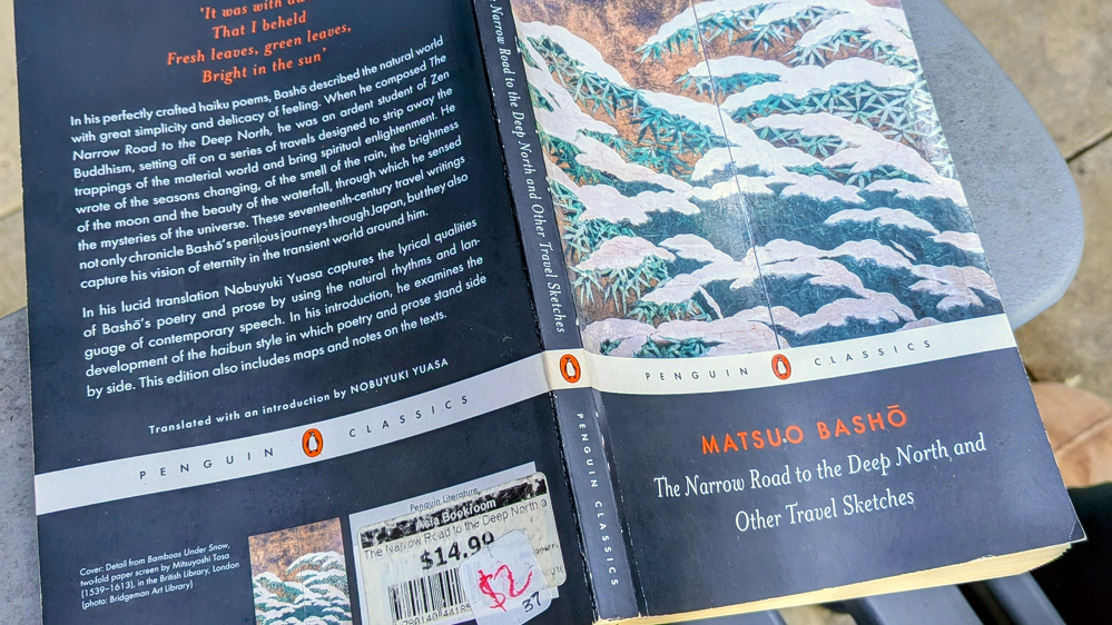 Auto-generated description: A paperback copy of The Narrow Road to the Deep North and Other Travel Sketches by Matsuo Bashō, part of the Penguin Classics series, is shown with a price sticker and detailed text on the cover.
