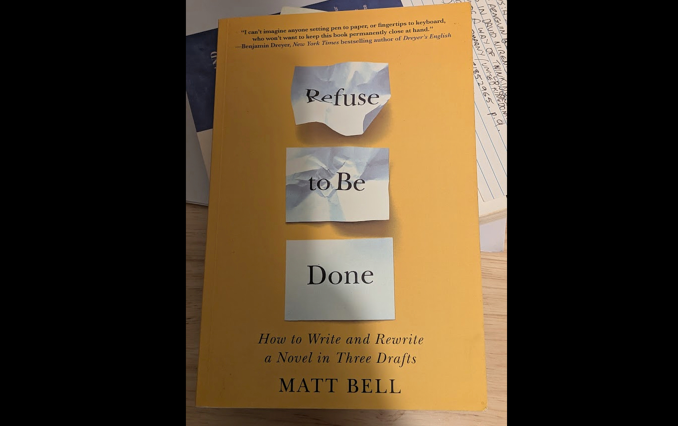 A book titled Refuse to Be Done: How to Write and Rewrite a Novel in Three Drafts by Matt Bell is shown on a desk.