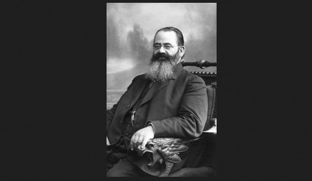 Semyon Vengerov, a bearded man in a suit, sits in an ornate chair, looking at the camera with a neutral expression.