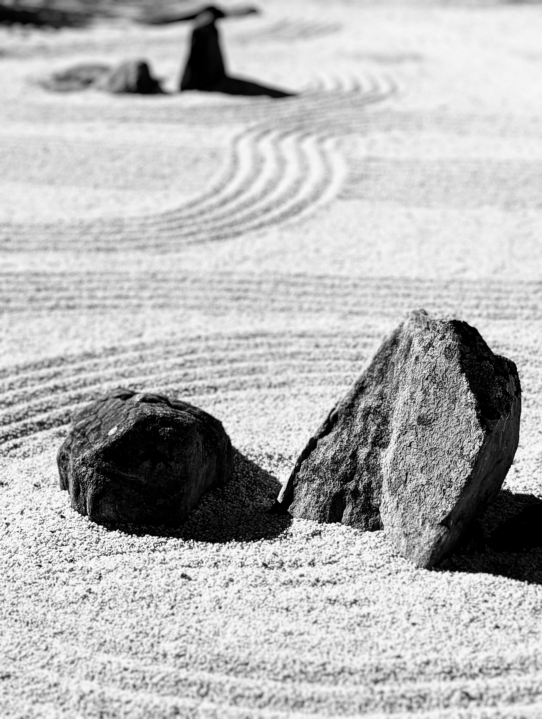 Two large stones are placed on finely raked sand with curved patterns in a minimalist Zen garden.