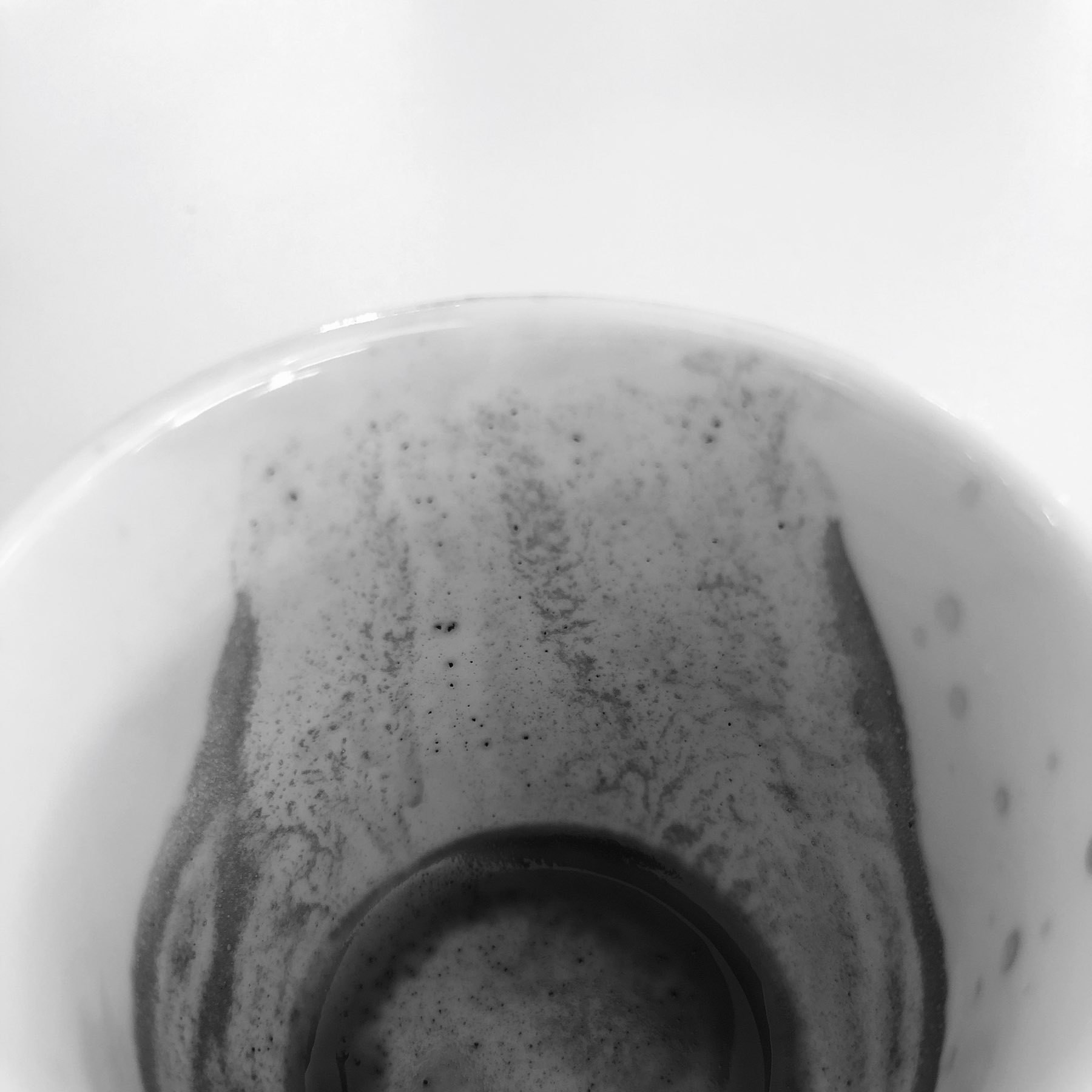 The black and white photo depicts a close-up view of an empty, white porcelain espresso cup, with remnants of a recently consumed espresso lining the inside of the cup.