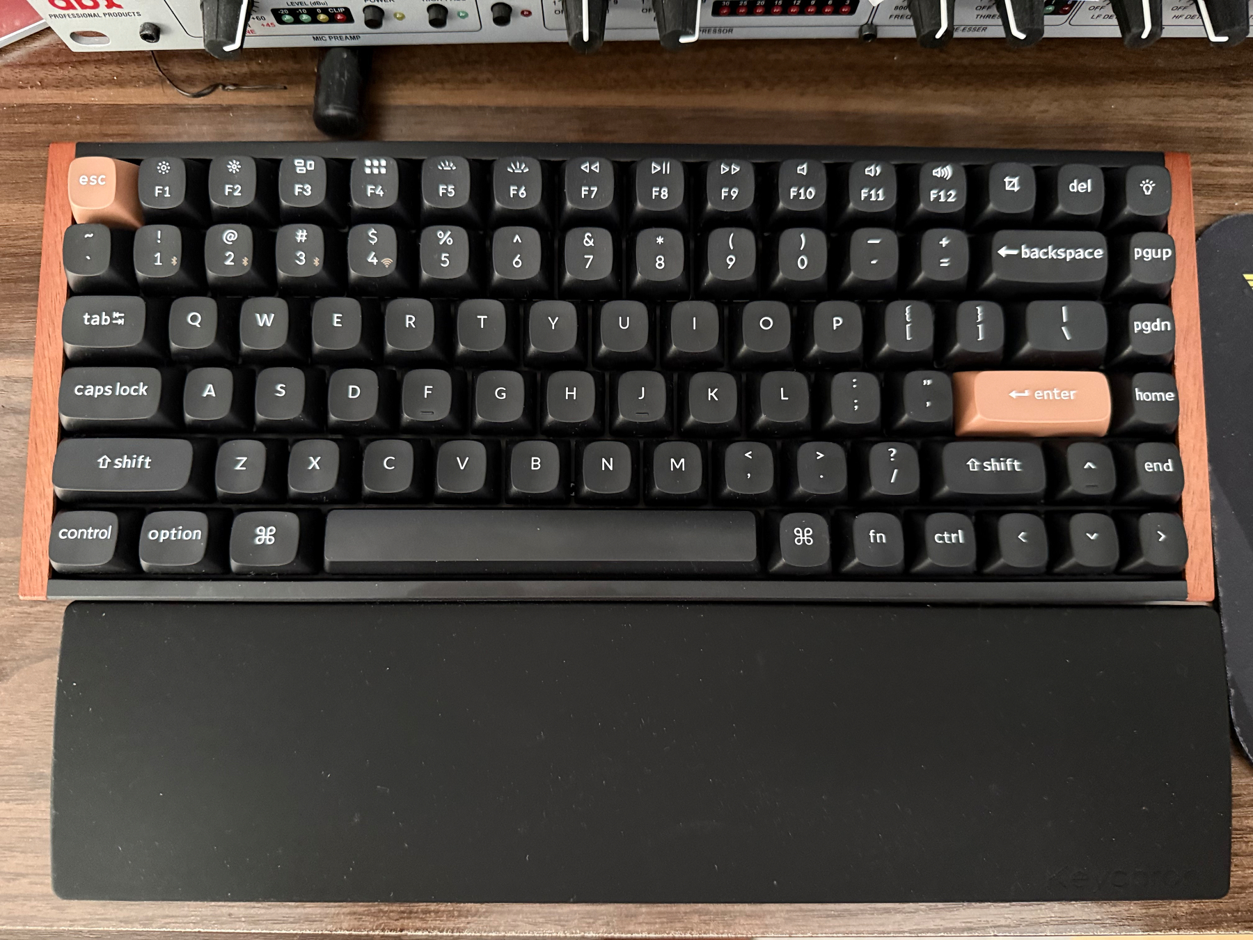 A black keyboard with a palmrest on a wood desk