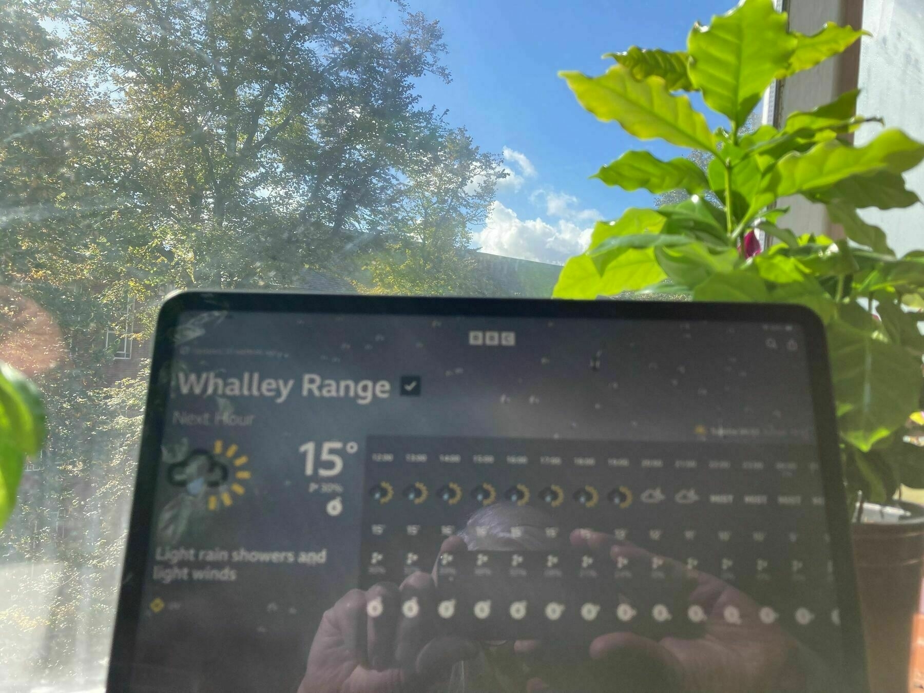 An iPad's weather app predicting a rainy day whilst there is blue sky and sunshine visible outside
