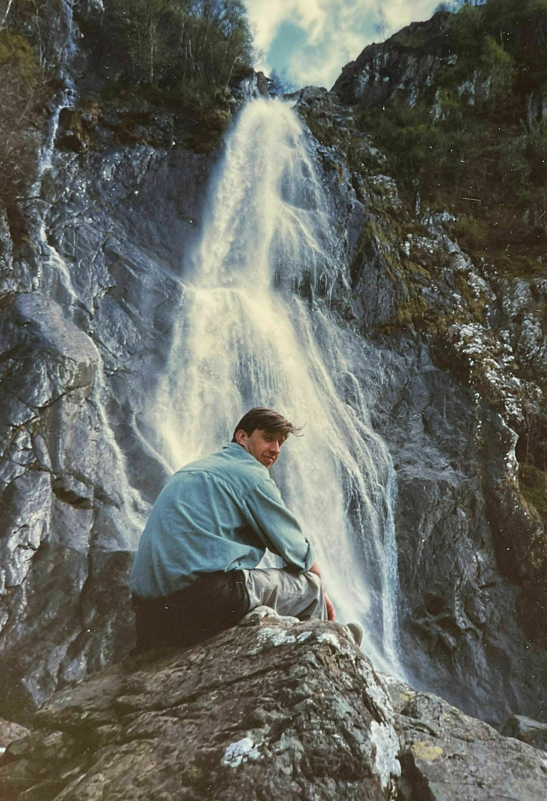 Man sitting on rocks beside a waterfall in Snowdonia, Wales, UK