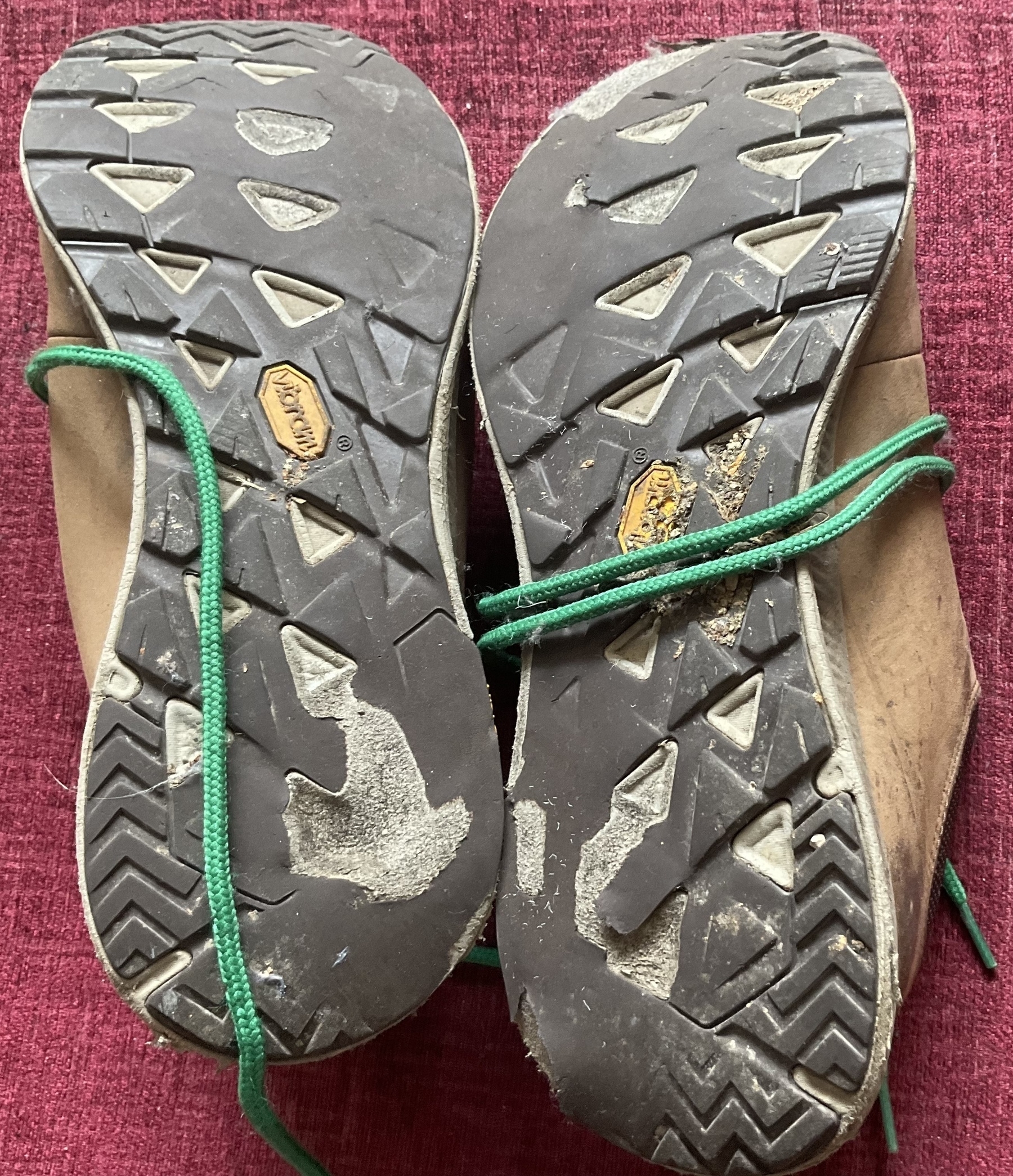 The severely worn soles of a pair of old walking shoes sporting a natty pair of green laces.