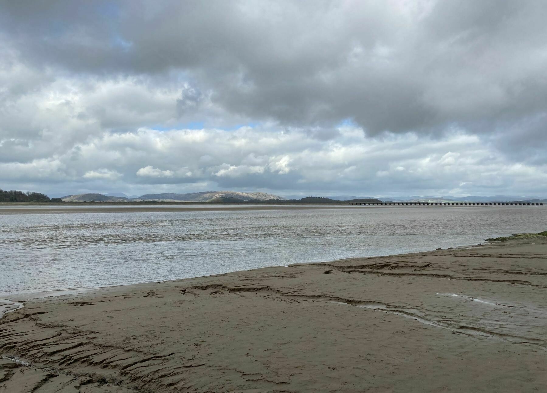 A view across the river Kent estuary at Arnside in the north west of the UK. The hills of the lake district can be seen on the far side and the railway viaduct crosses the river in the distance.