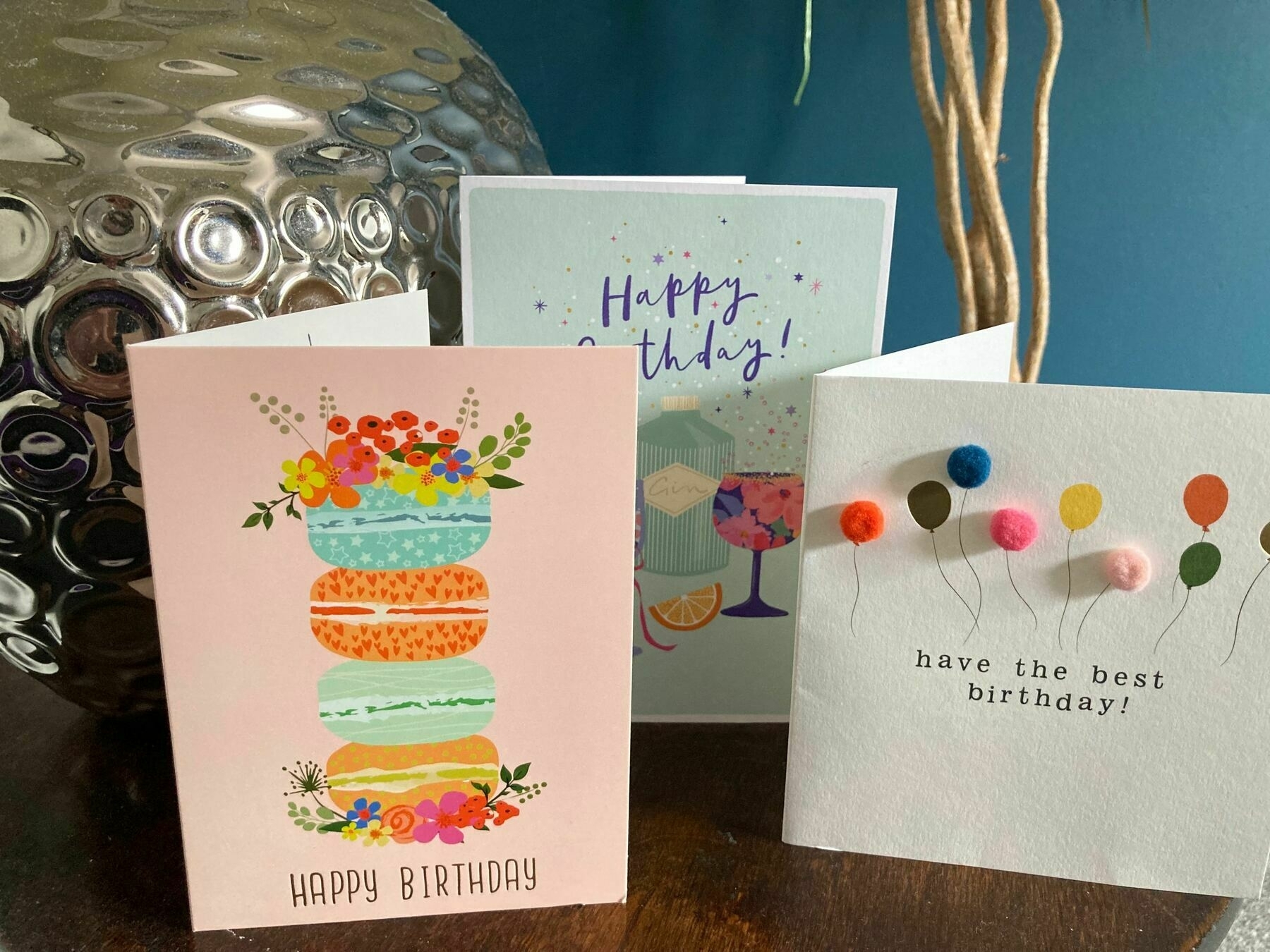 Three birthday cards standing on a shelf with a silvery ornament behind