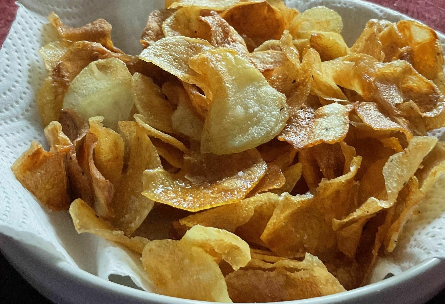 A bowl of  freshly made crisps glistening with hot oil.