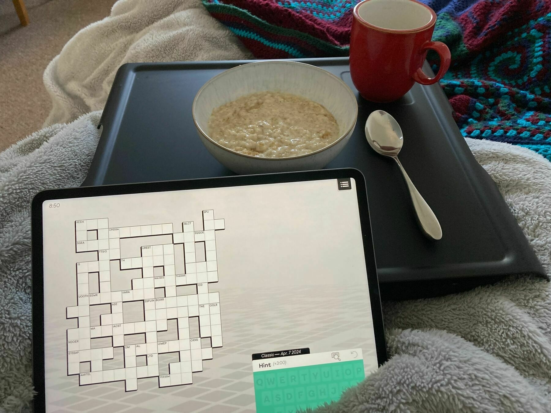 A tray with a mug bowl and spoon on a bed with an iPad ready to play the word game Knotwords.