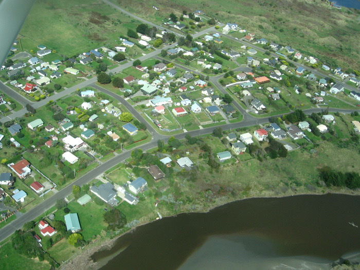 Aerial view of Waikawa village between and around Manga Pirau Street and Sarah Street, looking southeast, includes a section of coast.