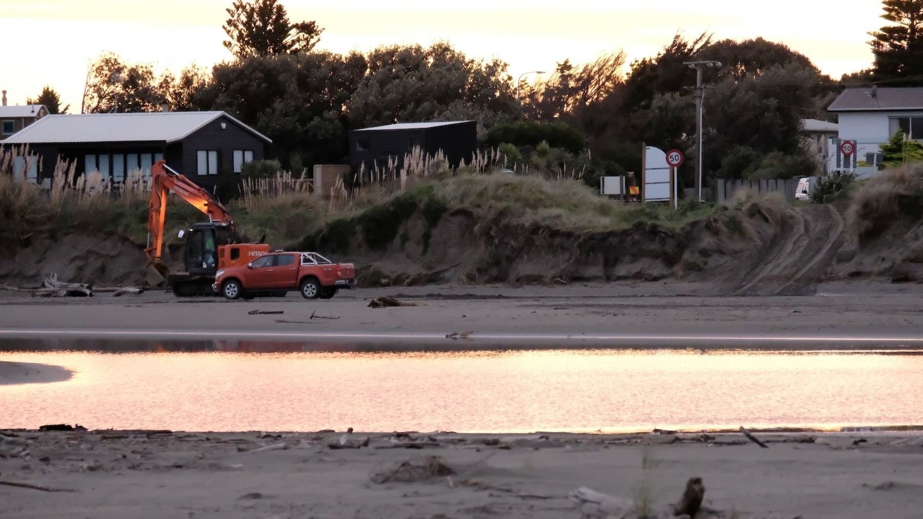 The digger arrived at dawn — on the beach near a car with sunlight reflected in water. 