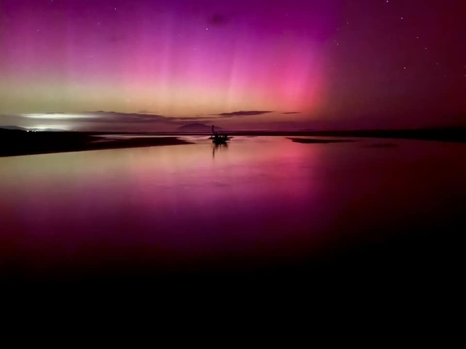 Yellow, pink, crimson aurora above the river flowing onto the beach. 