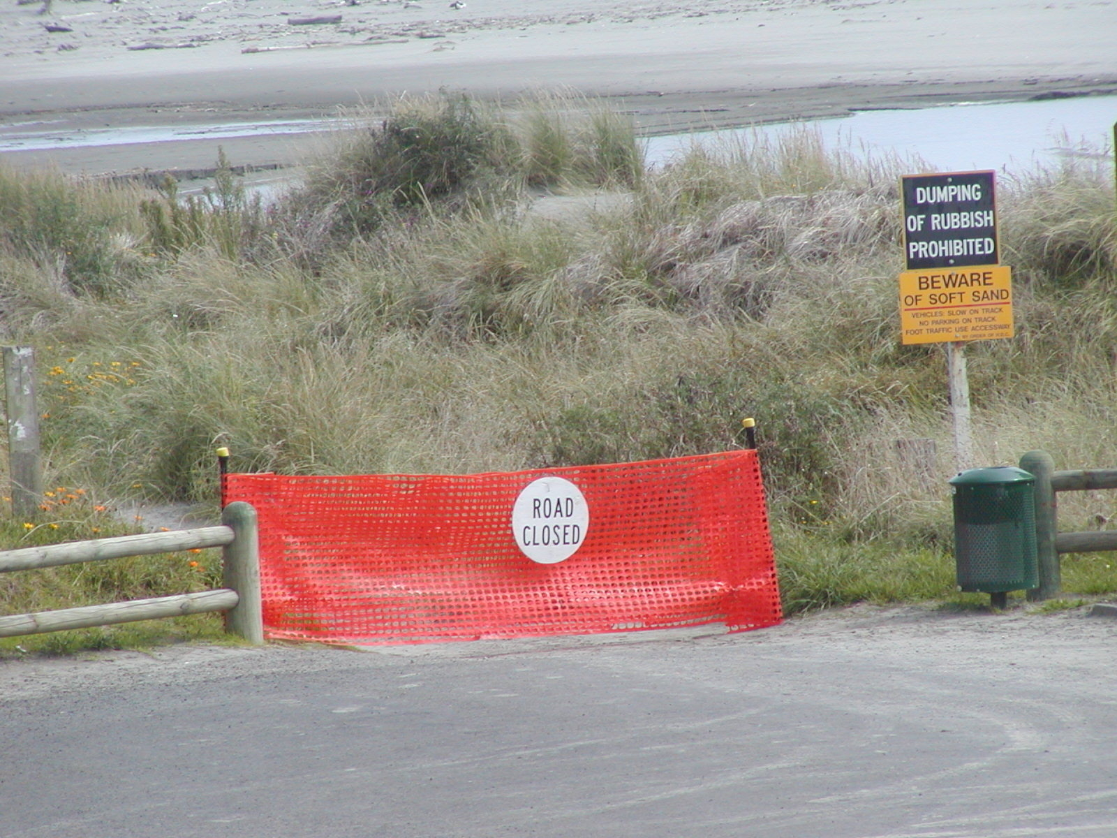 Red fabric fence across the beach access with a sign reading Road Closed. 