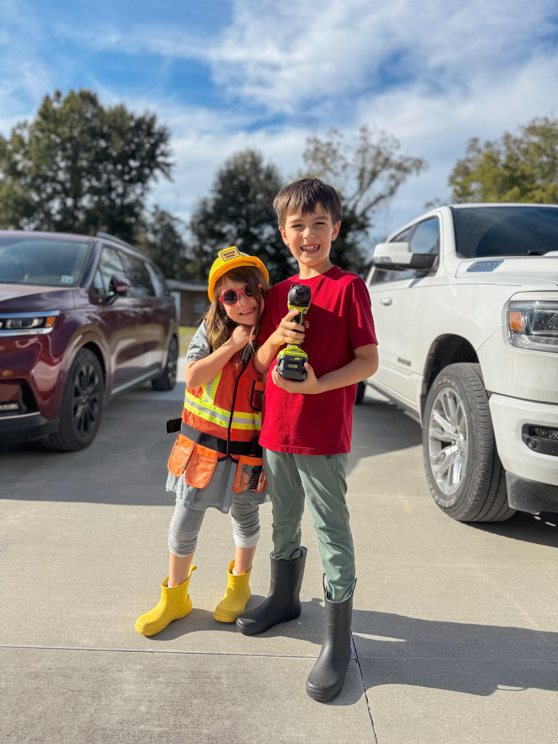 2 kids posing for a photo, 1 in a construction costume and the other holding a drill