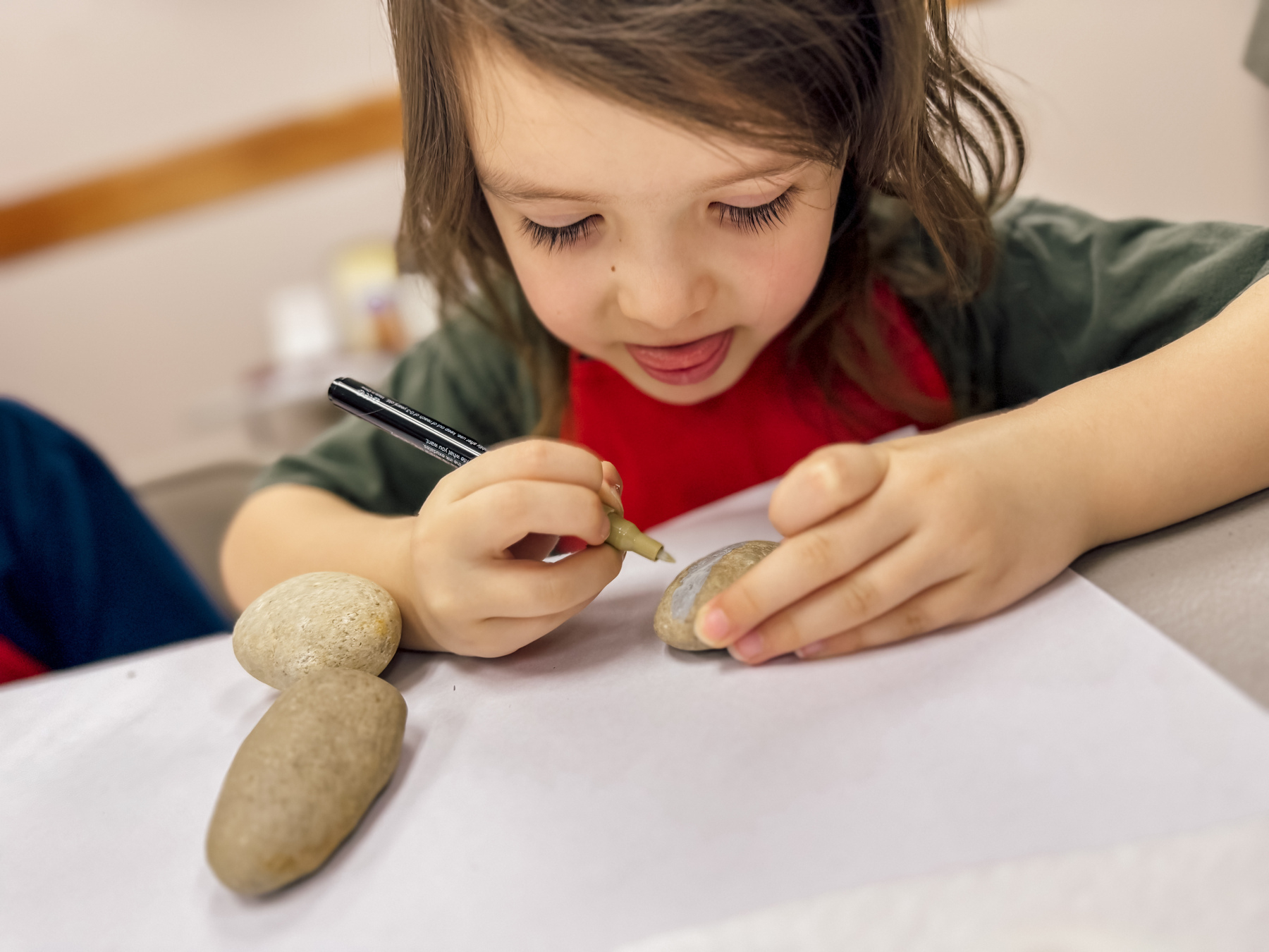 A young girl using an acrylic paint marker to decorate a river rock