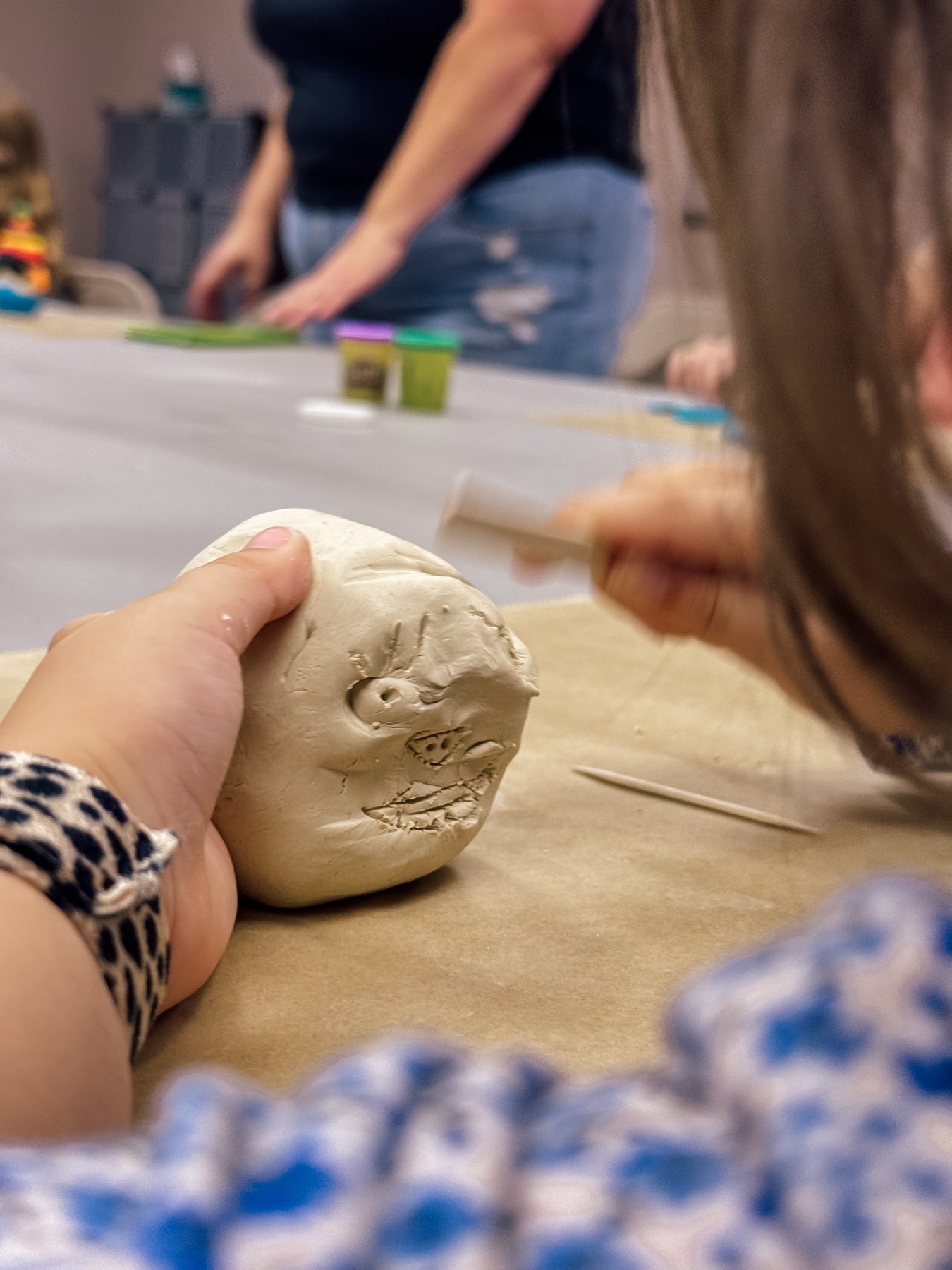 A child carving a face into clay shaped like a head