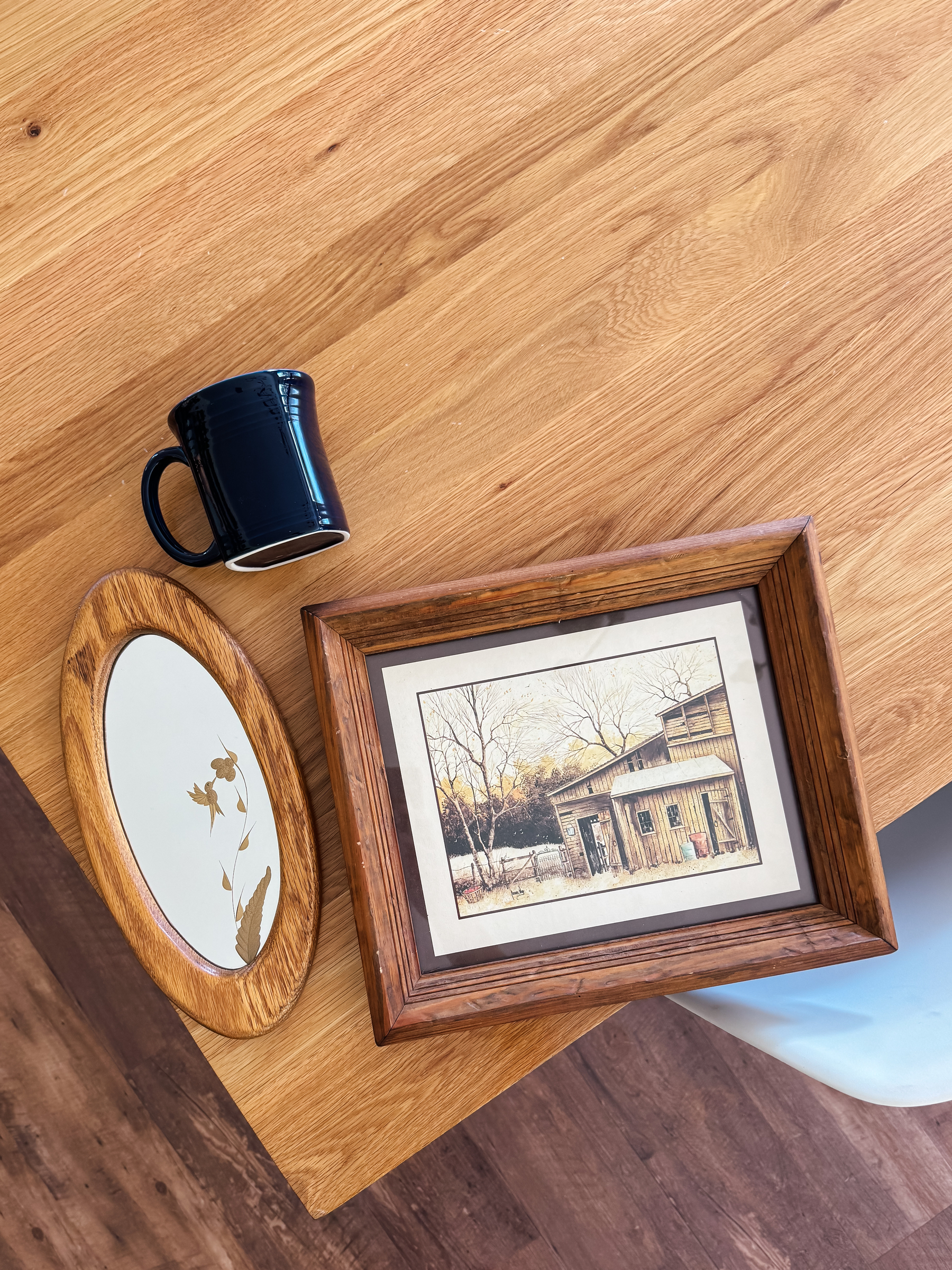 A thrifted oval mirror with an etched on hummingbird, a cobalt blue FiestawRe mug, and a framed old barn print